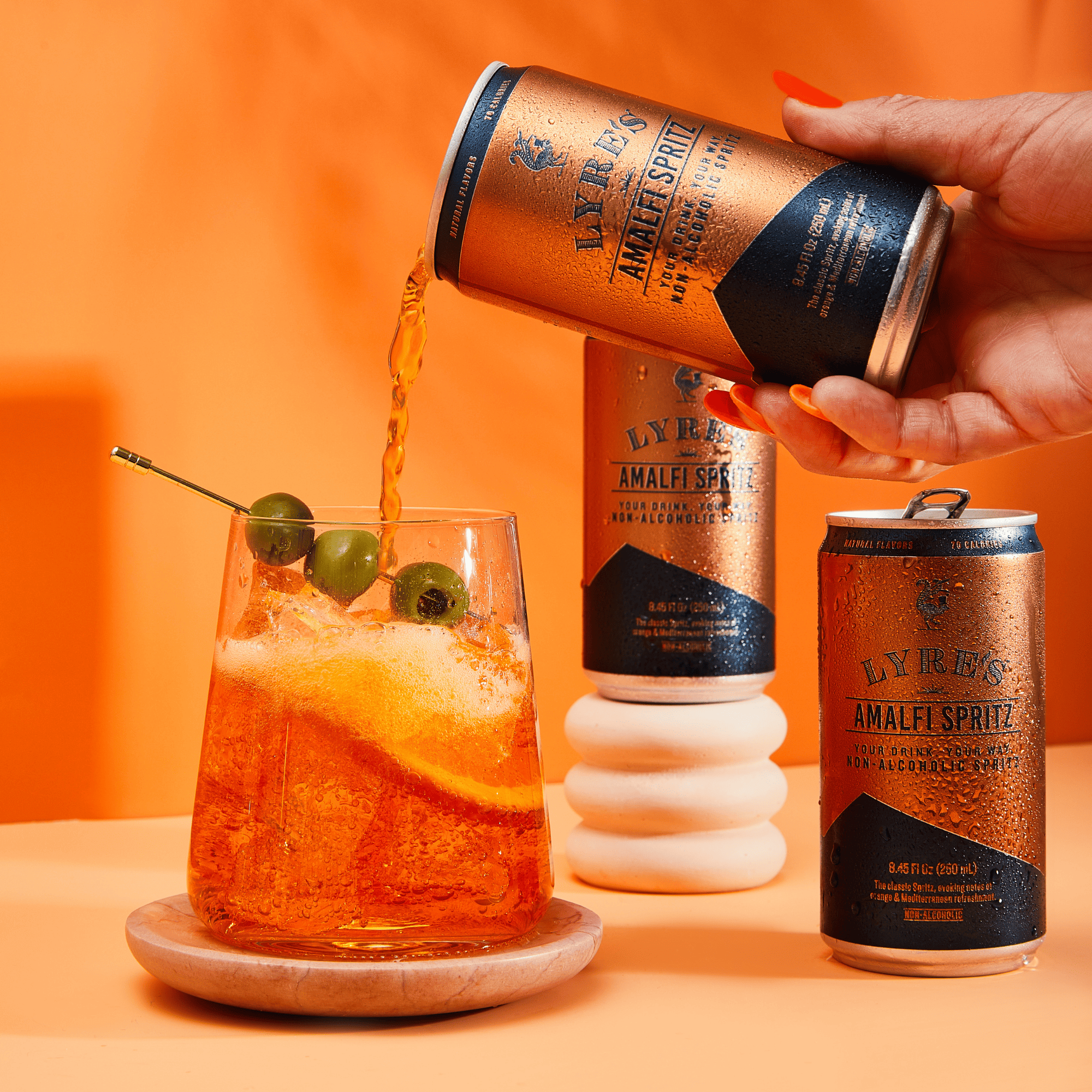 Person pouring Lyres Amalfi Spritz non alcoholic cocktail into a glass with an orange background
