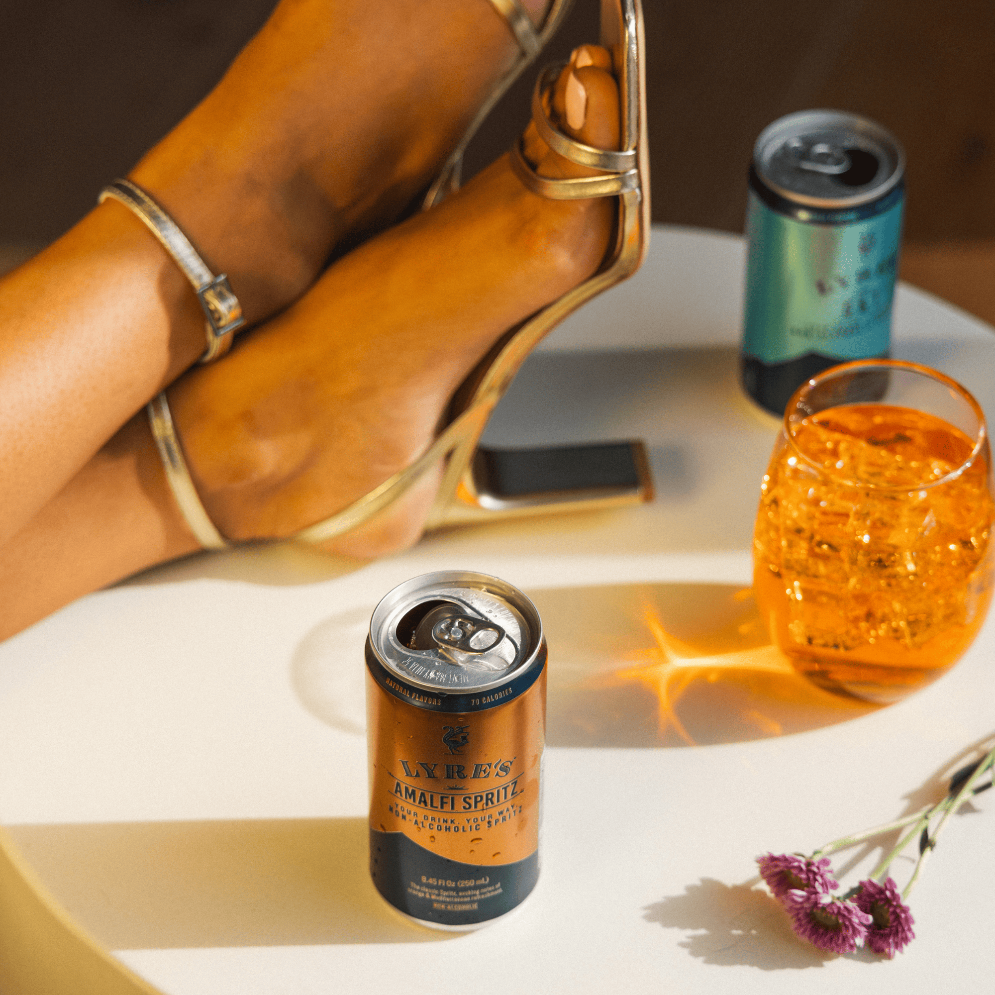 Can of Amalfi Spritz with a non alcoholic cocktail and high-heeled shoe on a table.