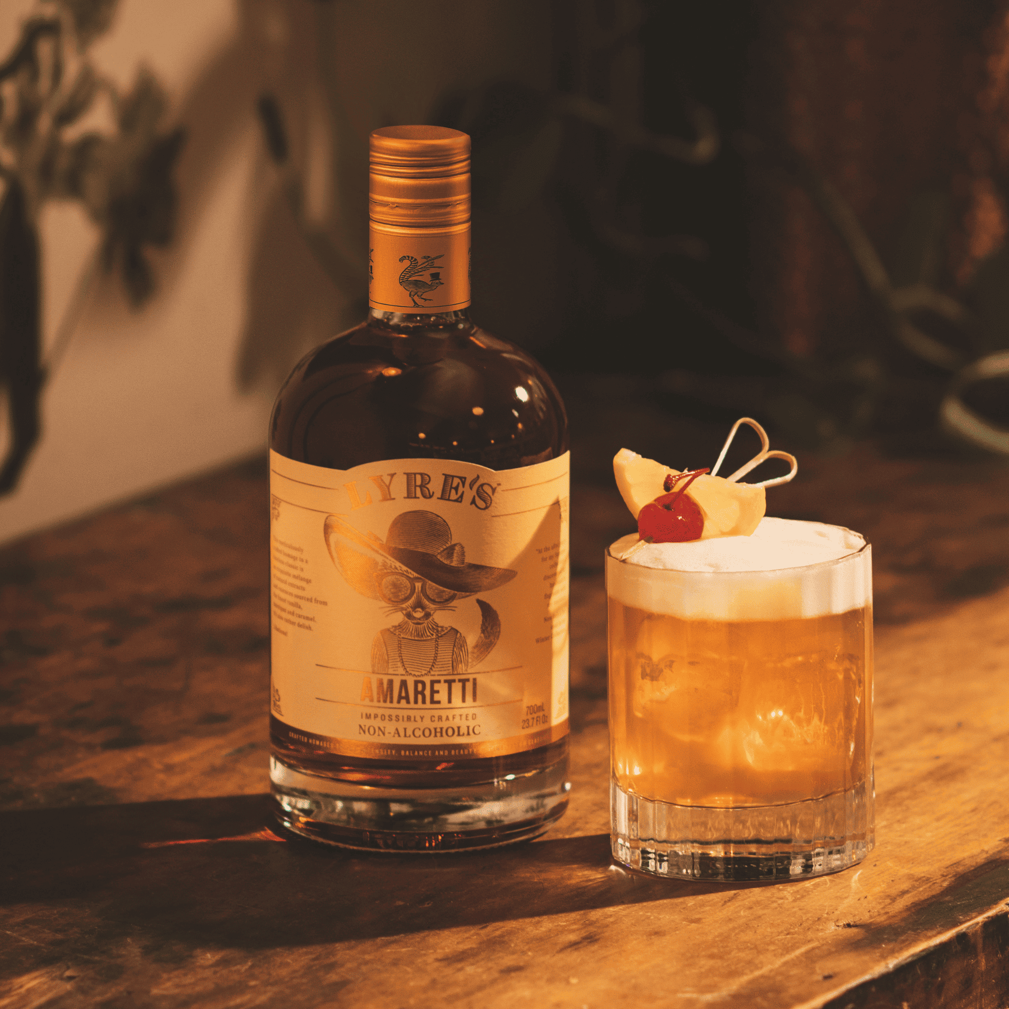 Bottle of Lyre's Amaretti non-alcoholic next to an Amaretti Sour cocktail with a cherry and pineapple on a wooden surface.