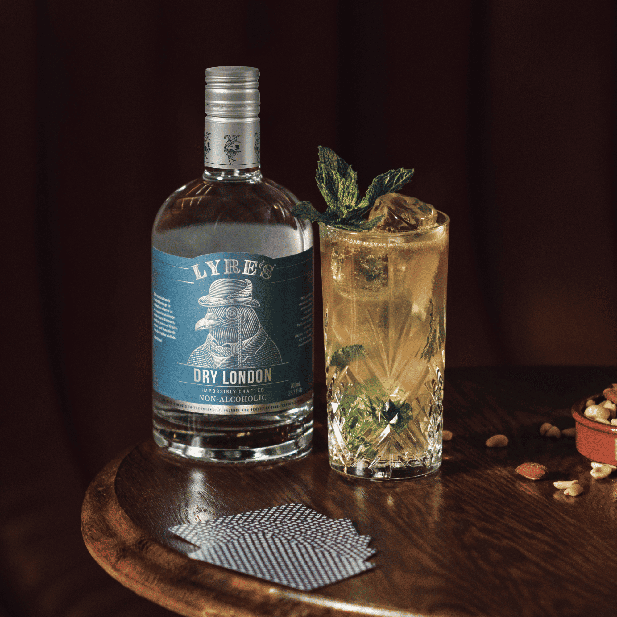 Lyre's Dry London non-alcoholic bottle with a Gin Gin Mule cocktail on a wooden surface next to a pack of cards
