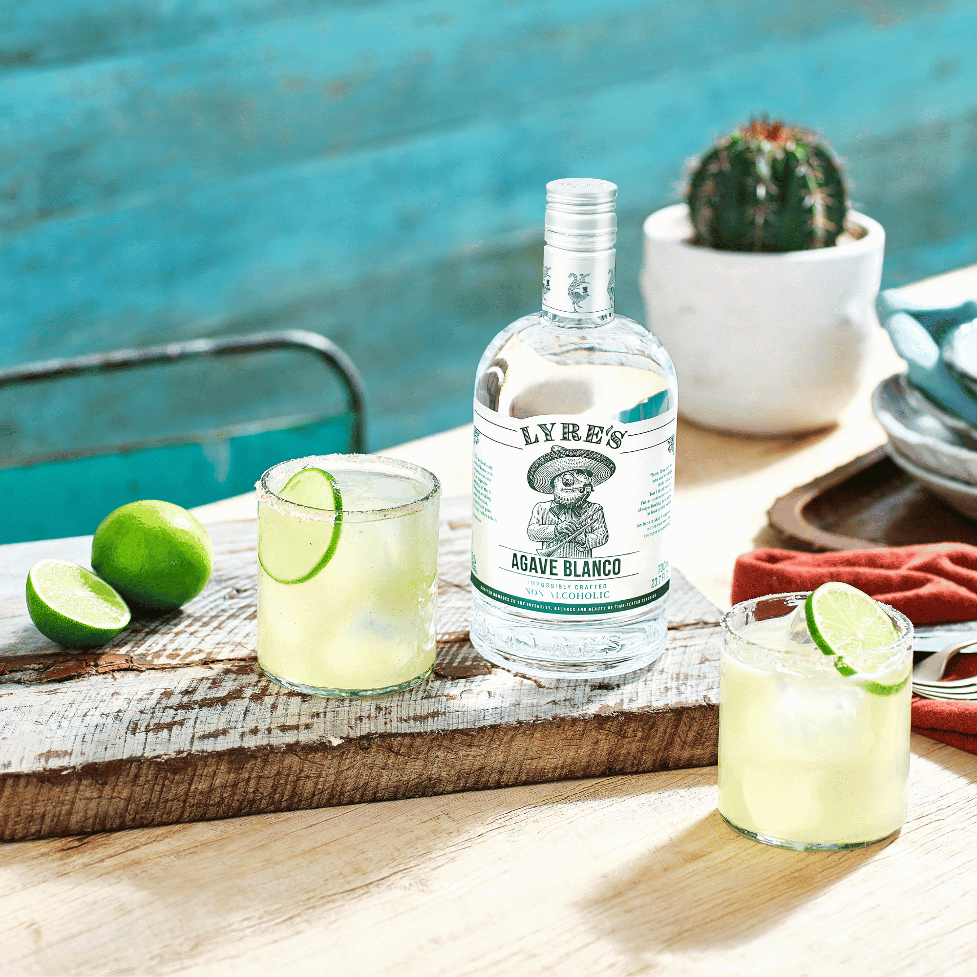 Lyre's Agave Blanco bottle with two margaritas on a wooden tray by a poolside.